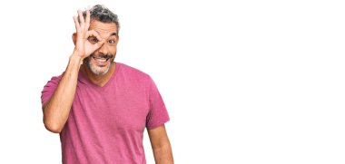 Orta yaşlı, gri saçlı, günlük kıyafetler giyen, el hareketleriyle gülümseyen, mutlu yüzüyle parmaklarının arasından bakan bir adam.. 