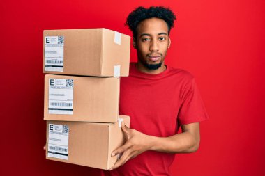 Sakallı, teslimat paketleri taşıyan Afro-Amerikalı genç adam yüzünde ciddi bir ifadeyle rahatladı. Basit ve doğal bir şekilde kameraya bakıyorsun.. 