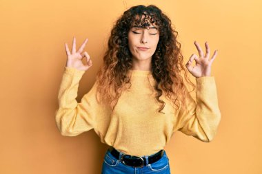 Gündelik kıyafetler giyen, gözleri kapalı gülümseyen genç İspanyol kız parmaklarıyla meditasyon hareketi yapıyor. yoga konsepti. 