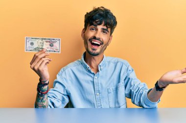 50 dolarlık banknotu elinde tutan İspanyol genç adam başarıyı mutlu bir gülümsemeyle kutluyor ve kazanan el kaldırarak ifade ediyor. 