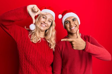 Yılbaşı şapkası takan, gülümseyen, elleri ve parmakları mutlu yüzlü genç bir çift. yaratıcılık ve fotoğrafçılık kavramı. 