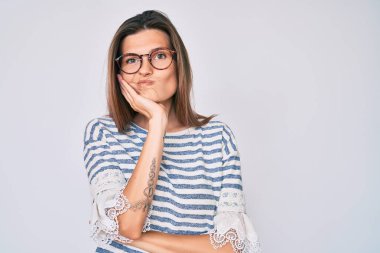 Güzel, beyaz bir kadın günlük kıyafetler ve gözlük takıyor. Kollarını kavuşturup depresyondan sıkılmış ve yorgun görünüyor.. 