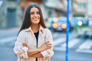 Çapraz kollu genç İspanyol kız şehirde mutlu gülümsüyor..