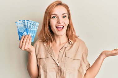 Genç beyaz kadın elinde 10000 Şili pezosu ile zaferi mutlu bir gülümseme ve kazanan bir ifadeyle kutluyor. 