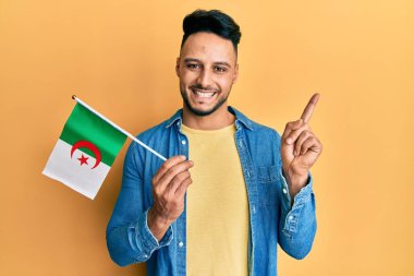 Cezayir bayrağını tutan genç Arap adam mutlu bir şekilde gülümsüyor. 