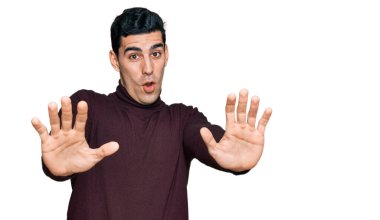 Balıkçı yaka kazak giyen yakışıklı İspanyol. Korkudan dehşete düşmüş ve korkmuş. El hareketlerini bırak, şok içinde bağır. panik konsepti. 