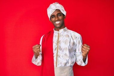 Sherwani elbisesi giyen yakışıklı Hintli adam başarı için heyecanlı kolları havada ve gözleri kapalı zaferi kutlarken gülümsüyor. Kazanan konsept. 