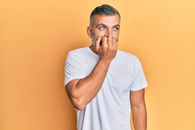 Orta yaşlı beyaz tişört giyen yakışıklı bir adam gergin ve gergin görünüyor. Ağzı tırnak yiyen eller. anksiyete. 