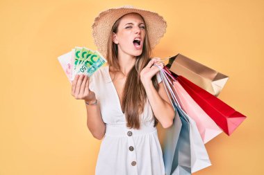 Alışveriş torbaları tutan genç sarışın kız ve İsrail şekelleri kızgın ve öfkeli çığlıklar atıyor öfkeyle bağırıyor. öfke ve agresif konsept. 