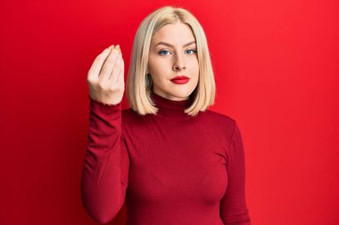 Genç sarışın kadın gündelik kıyafetler giyip İtalyan jesti yapıyor. El ve parmaklarıyla kendinden emin ifade ediyor. 