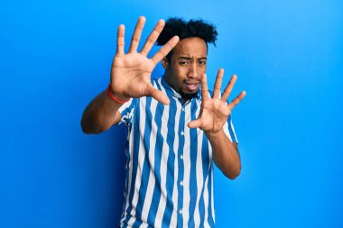 Sakallı, sıradan çizgili tişörtlü, korku ifadesinden korkan genç Afro-Amerikan bir adam. El kol hareketi yapmayı kes, şok içinde bağır. panik konsepti. 