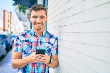 Beyaz adam şehirde akıllı telefon kullanarak mutlu bir şekilde gülümsüyor..