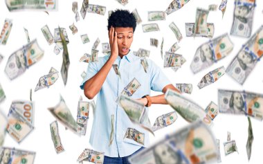 Gündelik giysiler giymiş genç Afro-Amerikan bir adam saatine bakıyor endişeli, geç kalmaktan korkuyor.