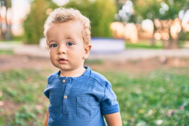 Sevimli ve mutlu küçük çocuk güneşli bir günde parkta eğleniyor. Güzel sarı saçlı erkek çocuk dışarıda oynuyor.