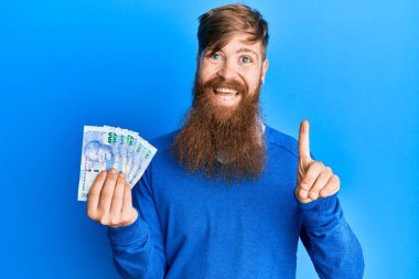 Genç İrlandalı kızıl saçlı adam Güney Afrika 'da 100 rand' lık banknotları elinde tutuyor. Bir fikir veya soruyla gülümsüyor ve gülümsüyor. 