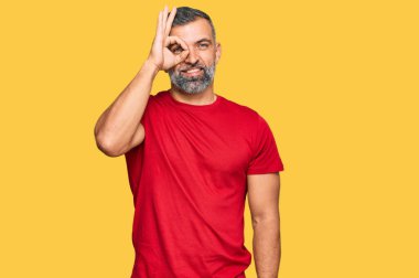 Orta yaşlı, sıradan kıyafetler giyen yakışıklı bir adam el hareketleriyle gülümseyen, mutlu yüzlü parmaklarından bakan bir jest yapıyor.. 