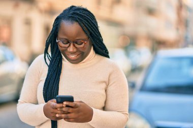 Genç Afrikalı Amerikalı kadın şehirde akıllı telefon kullanıyor..