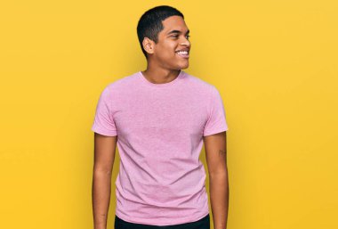 Genç, yakışıklı, günlük pembe tişört giyen, yüzünde gülümseme ve doğal ifadeyle yan yana bakan İspanyol bir adam. Kendinden emin gülen. 