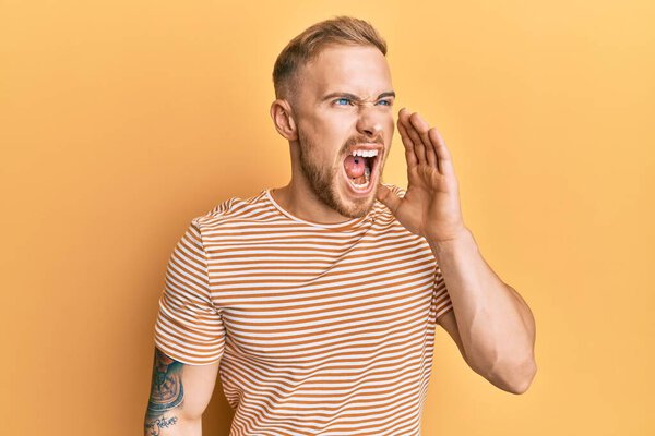 Молодой кавказский мужчина в обычной полосатой футболке кричал и громко кричал, прижав руку к рту. коммуникационная концепция. 