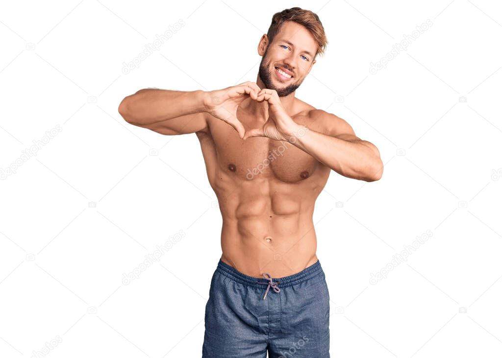 Young caucasian man standing shirtless smiling in love doing heart symbol shape with hands. romantic concept. 