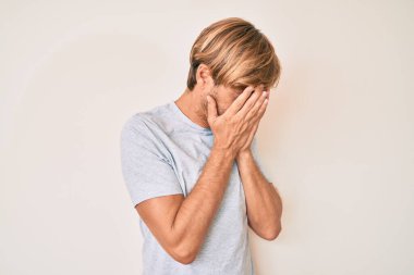 Ağlarken yüzünü ellerle kapatan, sıradan kıyafetler giyen genç sarışın bir adam. depresyon kavramı. 