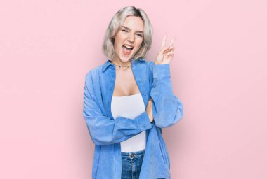 Sıradan kıyafetler giyen, gülümseyen, kameraya göz kırpan, zafer işareti yapan genç sarışın kız. İki numara.. 