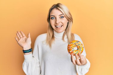 Genç, beyaz bir kadın elinde donut tutarak başarıyı mutlu bir gülümsemeyle kutluyor ve kazanan el kaldırarak ifade ediyor. 