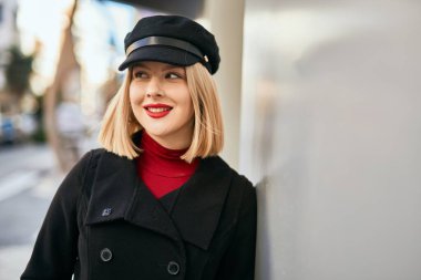 Genç sarışın kadın gülümsüyor, mutlu bir şekilde şehirde duruyor..