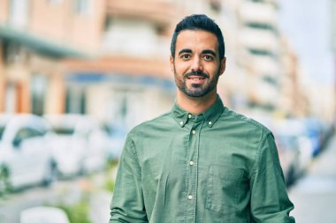 Genç İspanyol adam gülümseyerek şehirde mutlu mesut dikiliyor..