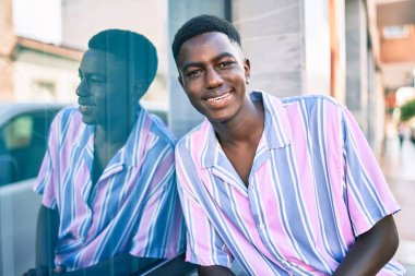 Genç Afrikalı Amerikalı gülümseyen mutlu bir adam şehrin duvarına yaslanıyor..