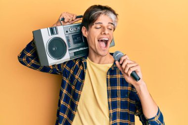 Genç İspanyol adam mikrofon ve teyp kullanarak şarkı söylüyor mutlu ve havalı bir gülümsemeyle gülümsüyor. diş gösterme. 