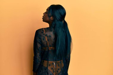 Genç Afrikalı Amerikalı kadın seksi iç çamaşırları giyiyor ve sarı arka planda ciddi ve baştan çıkarıcı bir yüzle poz veriyor.