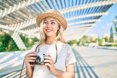 Beyaz tenli genç turist kız şehrin caddesinde klasik kamera kullanarak mutlu bir şekilde gülümsüyor..