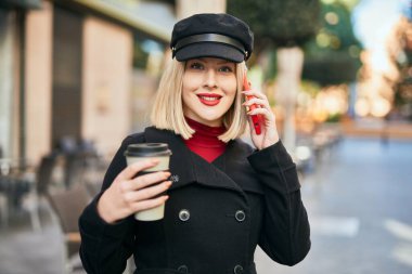 Genç sarışın kadın akıllı telefondan konuşuyor ve şehirde kahve içiyor..