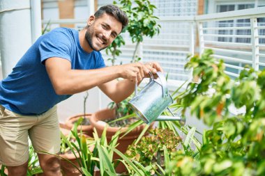 Genç yakışıklı adam gülümsüyor mutlu çiçekler terasta sulama tenekesi kullanıyor.