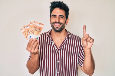 Avro banknotları tutan yakışıklı İspanyol bir adam bir fikir veya soruyla gülümsüyor ve mutlu bir yüzle işaret ediyor. 