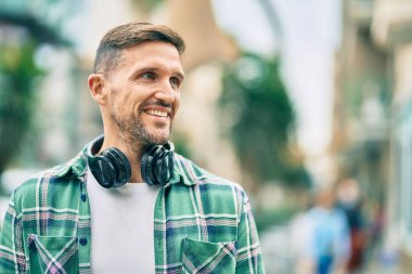 Genç beyaz adam şehirde kulaklık takarak mutlu bir şekilde gülümsüyor..