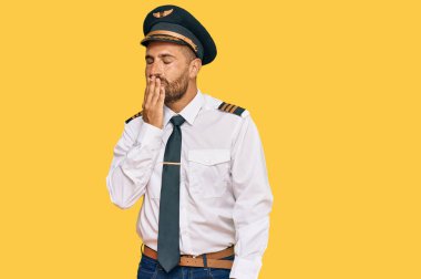 Uçak pilotu üniforması giyen sakallı yakışıklı bir adam ağzını eliyle kapatmaktan sıkılmış. Huzursuz ve uykulu.. 