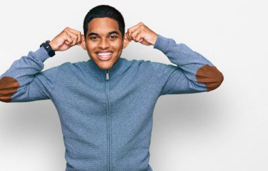 Genç, yakışıklı, sıradan bir kazak giyen, kulaklarını parmaklarıyla çeken, komik bir jest. deneme sorunu 