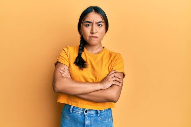 Gündelik kıyafetler giyen, kuşkucu ve gergin genç Latin bir kadın. Yüzünde çapraz kollarla onaylamayan bir ifade var. negatif kişi. 