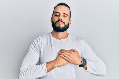 Sakallı, sıradan beyaz gömlekli, elleri göğsünde, gözleri kapalı, yüzünde minnet ifadesi olan genç bir adam. sağlık kavramı. 