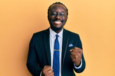 Yakışıklı, takım elbiseli ve kravatlı genç bir adam kolları havada ve gözleri kapalı bir şekilde başarıyı kutluyor. 