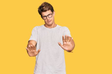 Yakışıklı beyaz adam, günlük kıyafetler ve gözlük takıyor, avuç içlerini hareket ettiriyor, reddediyor ve iğrenç bir ifadeyle reddediyor. Dur ve yasakla. 