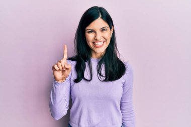 Genç İspanyol kadın gündelik kıyafetler giyip bir numarayı gösterip işaret ederken kendinden emin ve mutlu bir şekilde gülümsüyor.. 