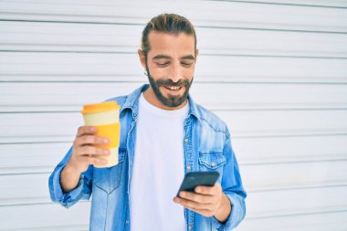 Ortadoğulu genç adam akıllı telefon kullanıyor ve içki içiyor. Şehirde kahve içiyor..