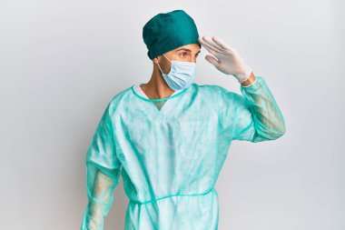 Cerrah üniforması ve tıbbi maske takan yakışıklı genç adam çok mutlu ve gülümsüyor. arama kavramı. 