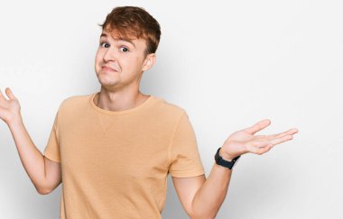 Sıradan kıyafetler giyen, kafası karışmış, elleri ve kolları havada genç beyaz bir adam. şüphe kavramı. 