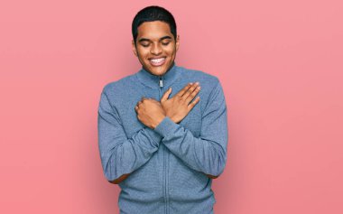 Genç, yakışıklı, sıradan bir kazak giyen, elleri göğsünde, gözleri kapalı gülümseyen ve yüzünde minnet ifadesi olan İspanyol bir adam. sağlık kavramı. 