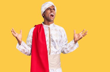 Geleneksel Sherwani elbisesi giyen Afrikalı yakışıklı adam deli gibi bağırıyor, bağırıyor ve agresif bir ifadeyle kollarını kaldırıyor. hüsran kavramı. 