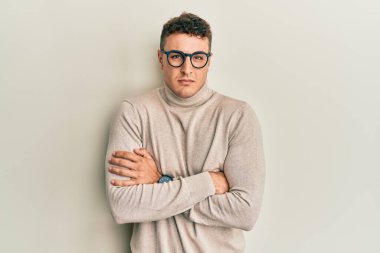 Balıkçı yaka kazak giyen İspanyol genç adam kış soğuğu için titriyor ve donuyor. Yüzünde üzgün ve şok ifadesi var. 